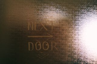 A glass panel on a door in The Nicholas Building, with a sign pointing to the right saying 'Next door'.